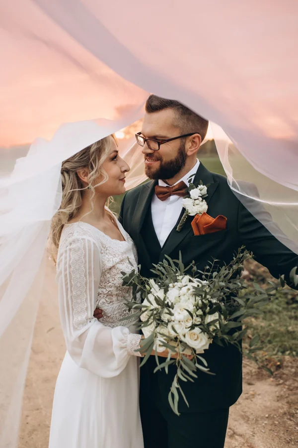 A wedding couple beneath a veil in the evening light, photographed by Baïba